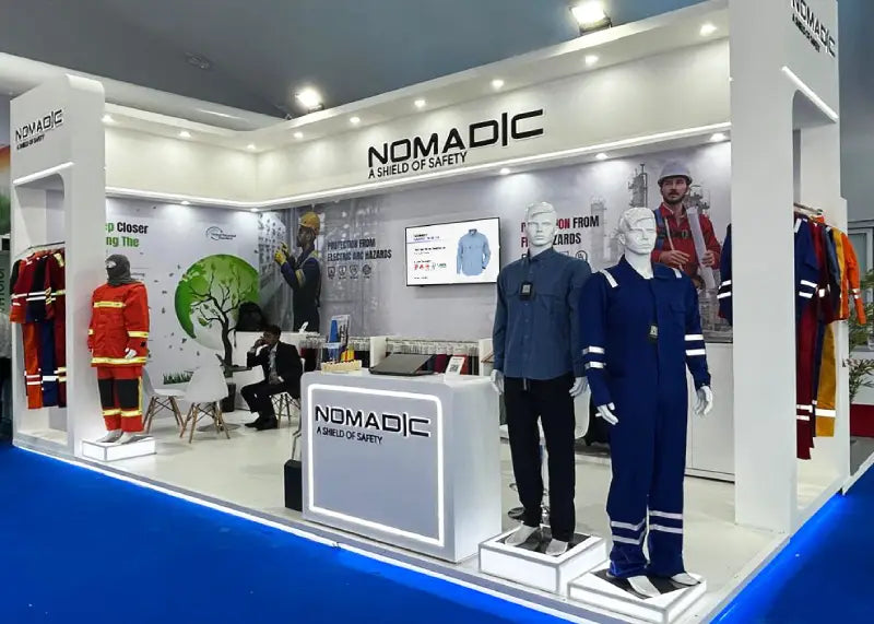 Nomadic side view booth at ADIPEC 2025 featuring mannequins in Oil & Gas FR/IFR coveralls and a display screen with product details.